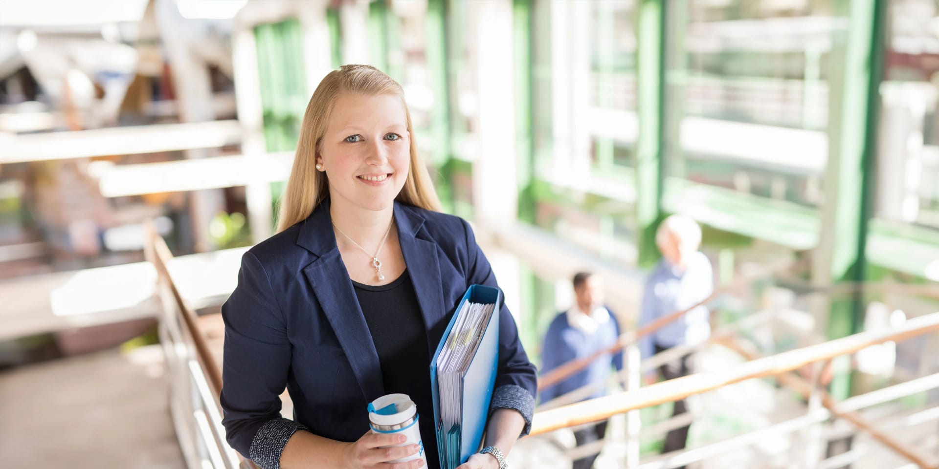 An employee with a file folder and a drinking cup in the stairwell at Uniper.